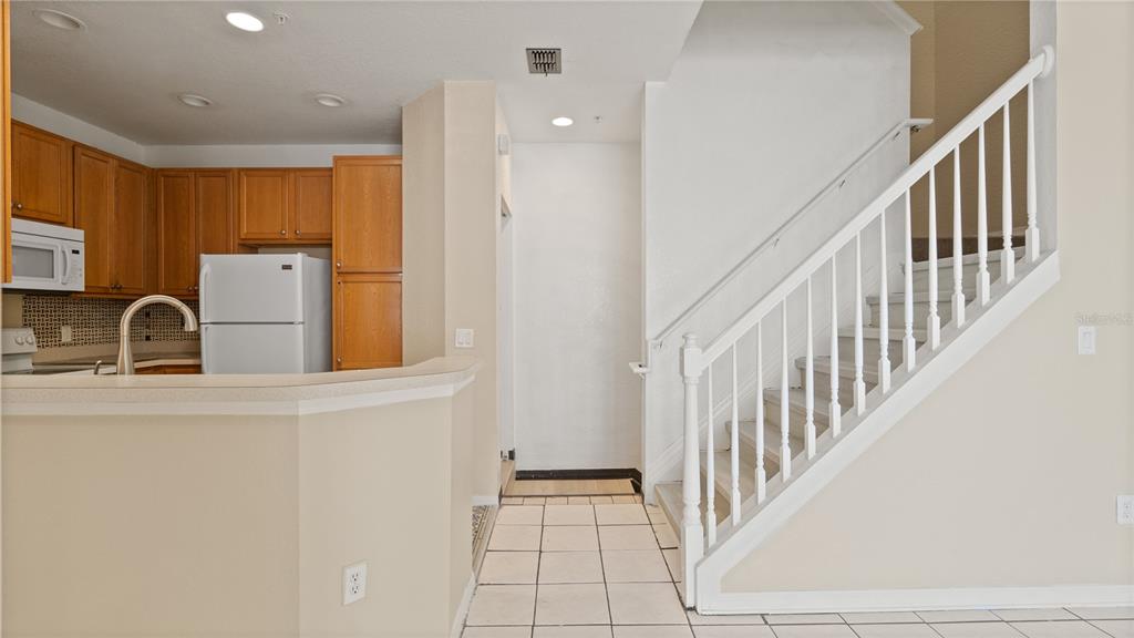 A kitchen with wood cabinets and a white refrigerator sits beside a carpeted staircase — 2586 GRAND CENTRAL PARKWAY UNIT 3, ORLANDO, FL