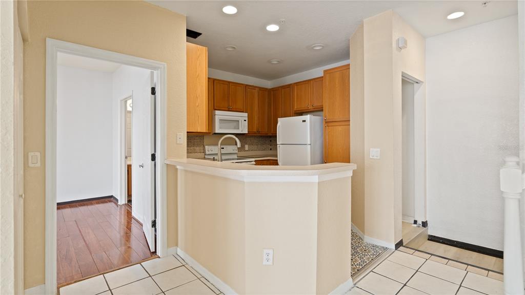A kitchen with wood cabinets, white appliances, and a breakfast bar overlooks a tiled floor — 2586 GRAND CENTRAL PARKWAY UNIT 3, ORLANDO, FL