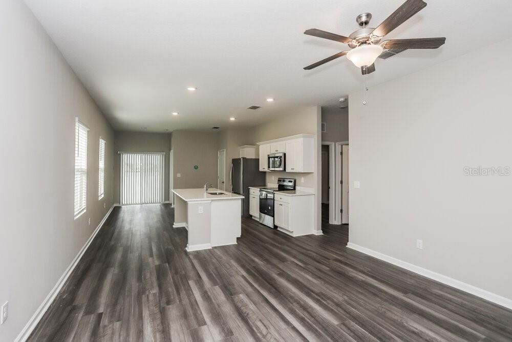 An open-concept kitchen and living area featuring white cabinetry, a center island, and wood-look flooring — 966 KELLY FERN LOOP, RUSKIN, FL