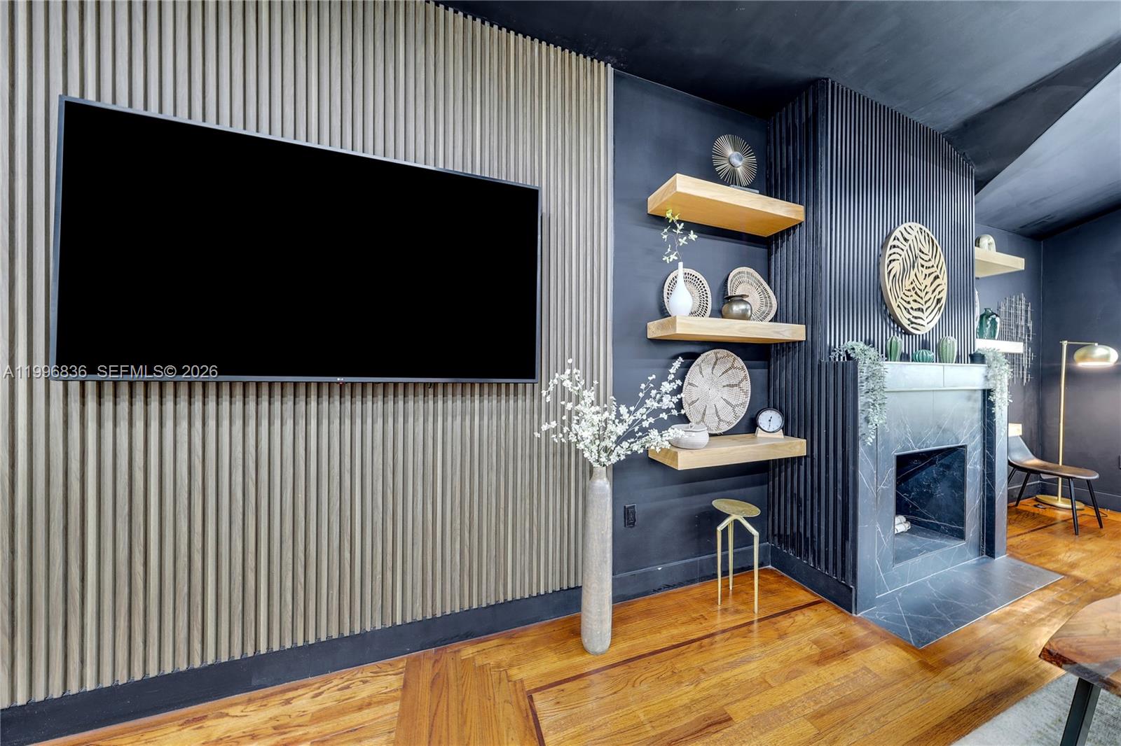 A living room features a wall-mounted television, wooden slat paneling, floating shelves, and a fireplace — 2612 SW 12th St, Miami FL 33135, MIAMI, FL