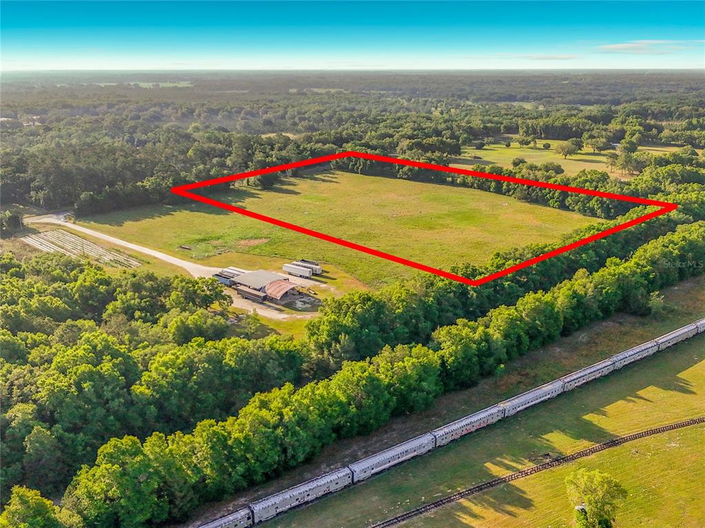 An aerial view shows a large, rectangular grassy field outlined in red near a train — TBD NE 195TH AVENUE, WILLISTON, FL