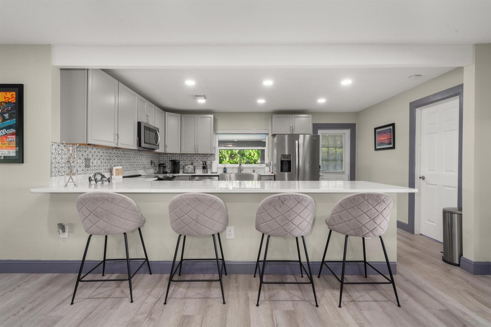 A kitchen features gray cabinets, a white countertop, four bar stools, and light wood flooring — 1622 W Dinner Lake Drive, Sebring FL 33870, SEBRING, FL
