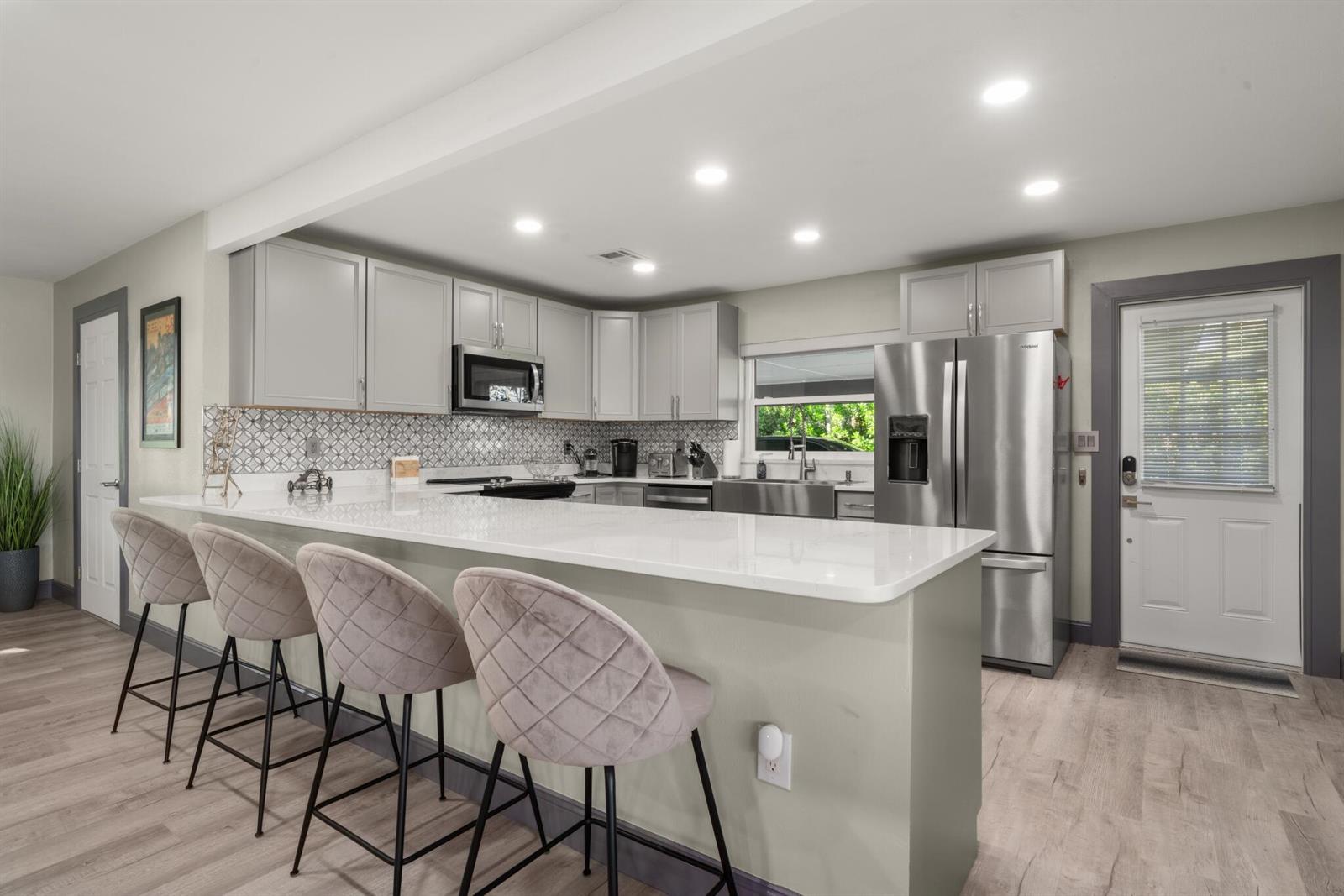 A kitchen features gray cabinets, a white quartz countertop, bar seating, and stainless steel appliances — 1622 W Dinner Lake Drive, Sebring FL 33870, SEBRING, FL