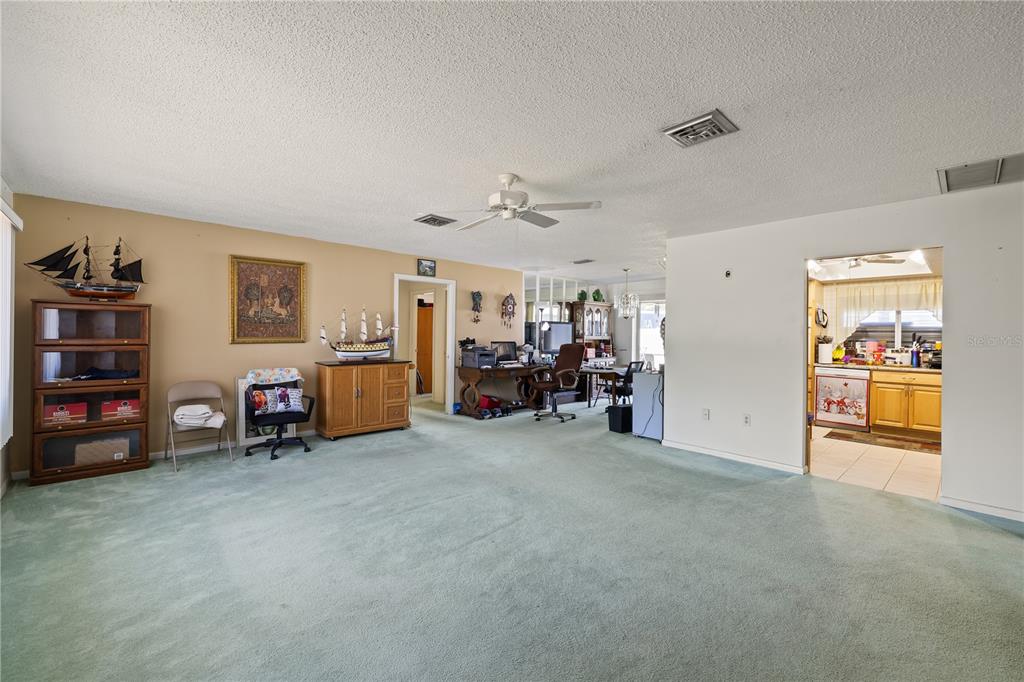 A spacious living area with light green carpeting, tan walls, and an open kitchen doorway — 22158 RIVERHEAD AVENUE, PORT CHARLOTTE, FL
