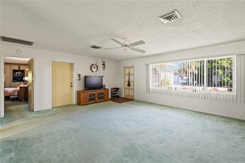 A living room features green wall-to-wall carpeting, a ceiling fan, and a large window — 22158 RIVERHEAD AVENUE, PORT CHARLOTTE, FL