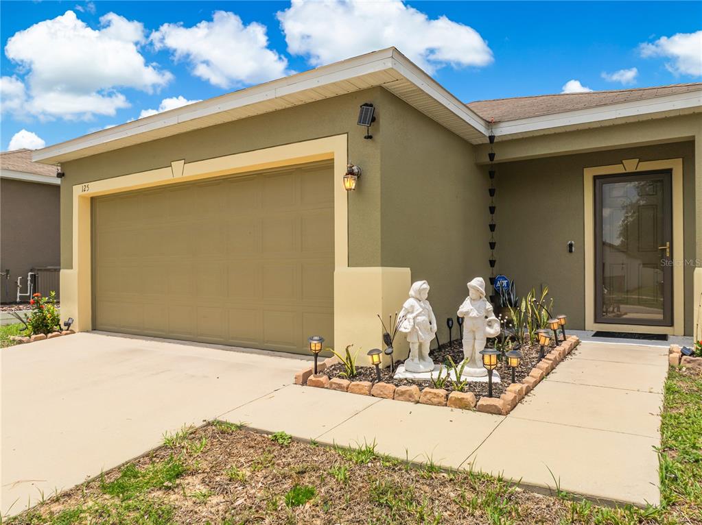 The exterior of a house features a tan garage, a front entrance, and garden statues — 125 TANAGER STREET, HAINES CITY, FL