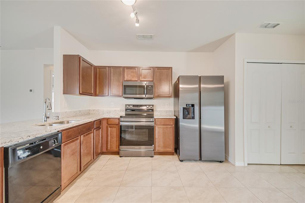 A kitchen features wood cabinets, stainless steel appliances, granite countertops, and light tile flooring — 125 TANAGER STREET, HAINES CITY, FL