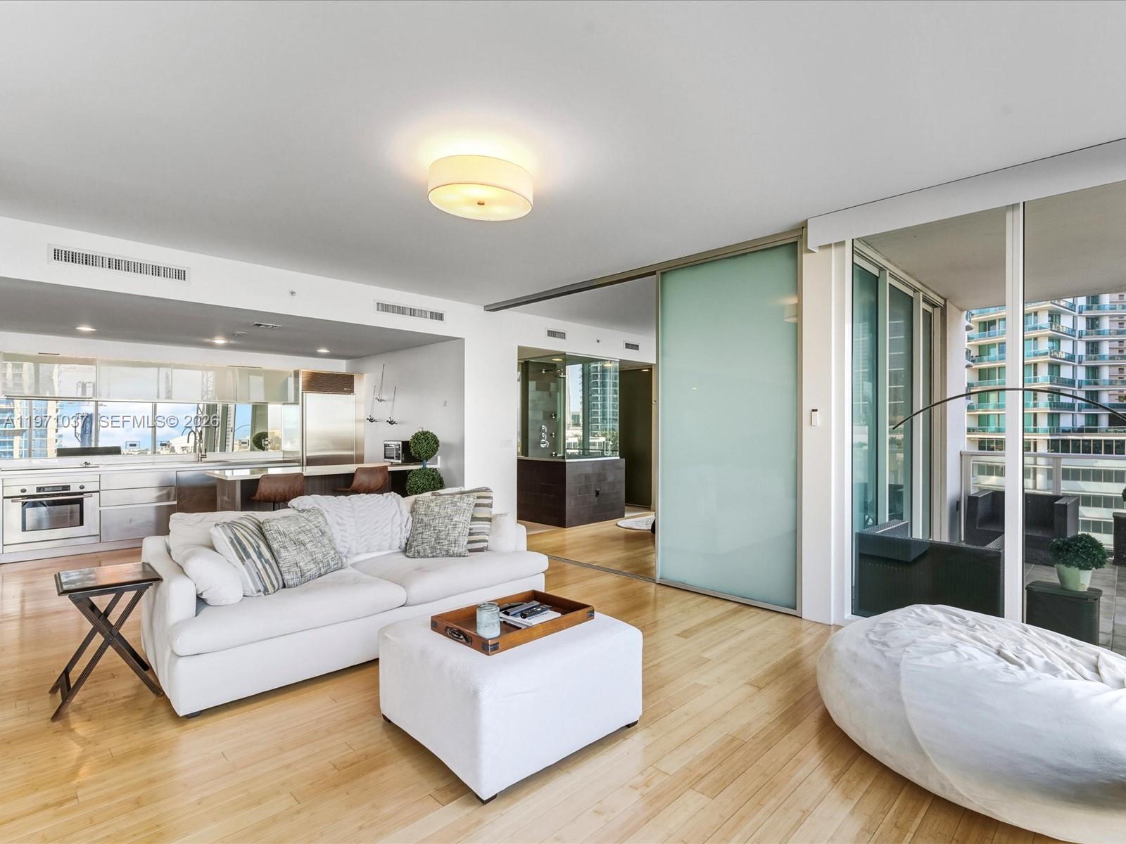A living room with light wood floors, a white sofa, and a sliding glass door — 1040 Biscayne Blvd # 1107, Miami FL 33132, MIAMI, FL