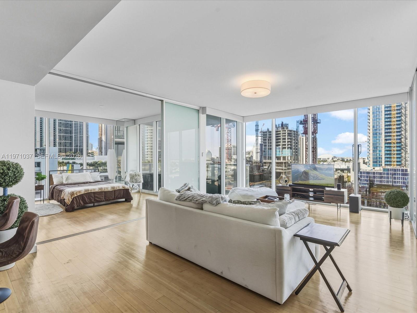 A modern living room and bedroom area with floor-to-ceiling windows overlooking a city construction site — 1040 Biscayne Blvd # 1107, Miami FL 33132, MIAMI, FL