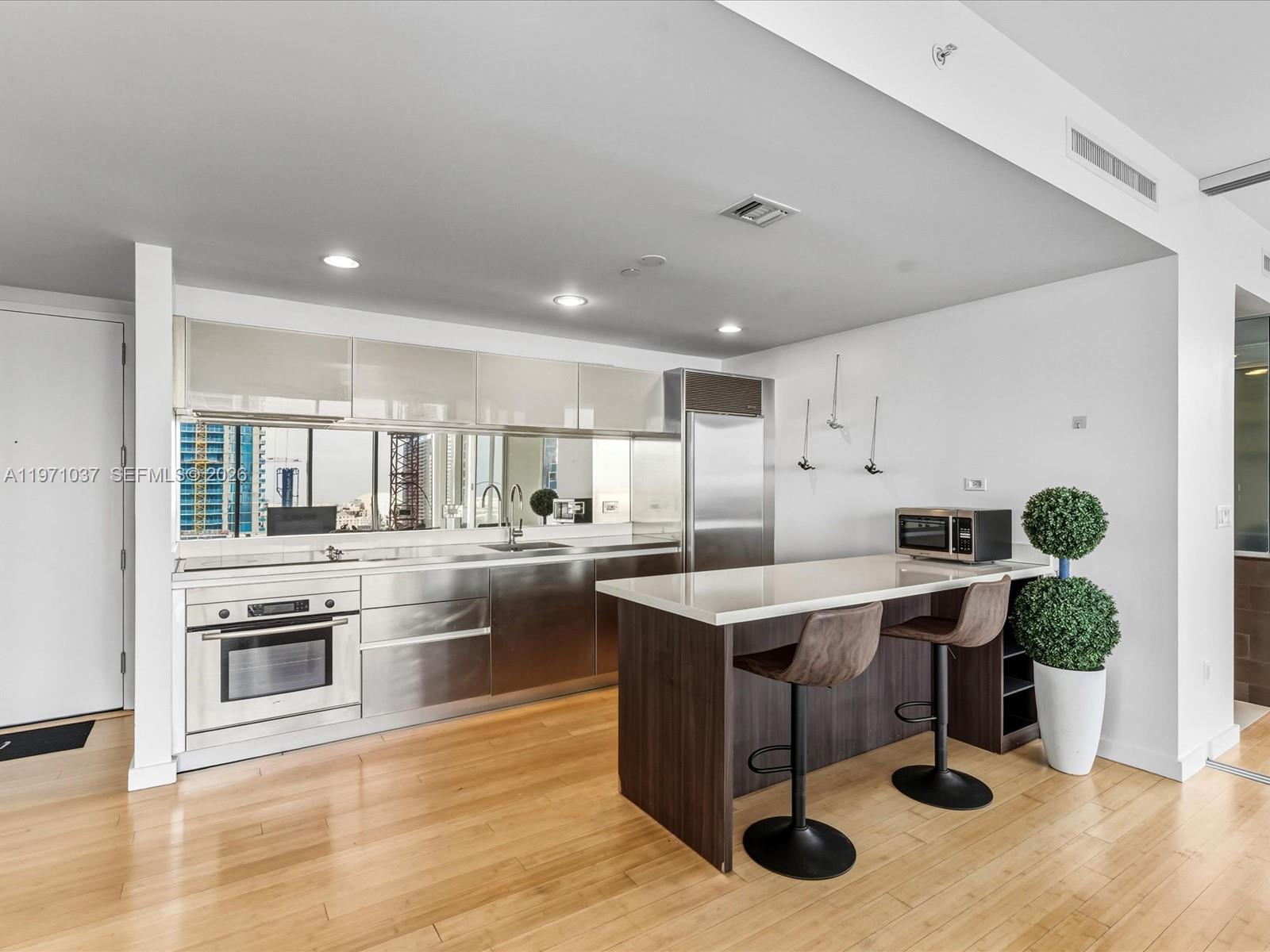 A modern kitchen features stainless steel cabinetry, a white island with bar stools, and hardwood floors — 1040 Biscayne Blvd # 1107, Miami FL 33132, MIAMI, FL