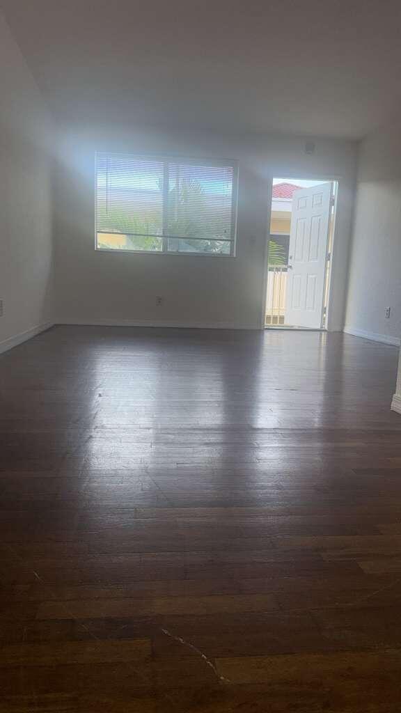 An empty room with dark wood flooring, a window with blinds, and an open door — NORTH MIAMI BEACH, FL