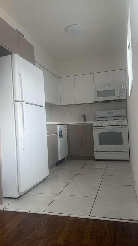 A kitchen features white appliances, two-toned cabinetry, white countertops, and light-colored floor tiles — NORTH MIAMI BEACH, FL
