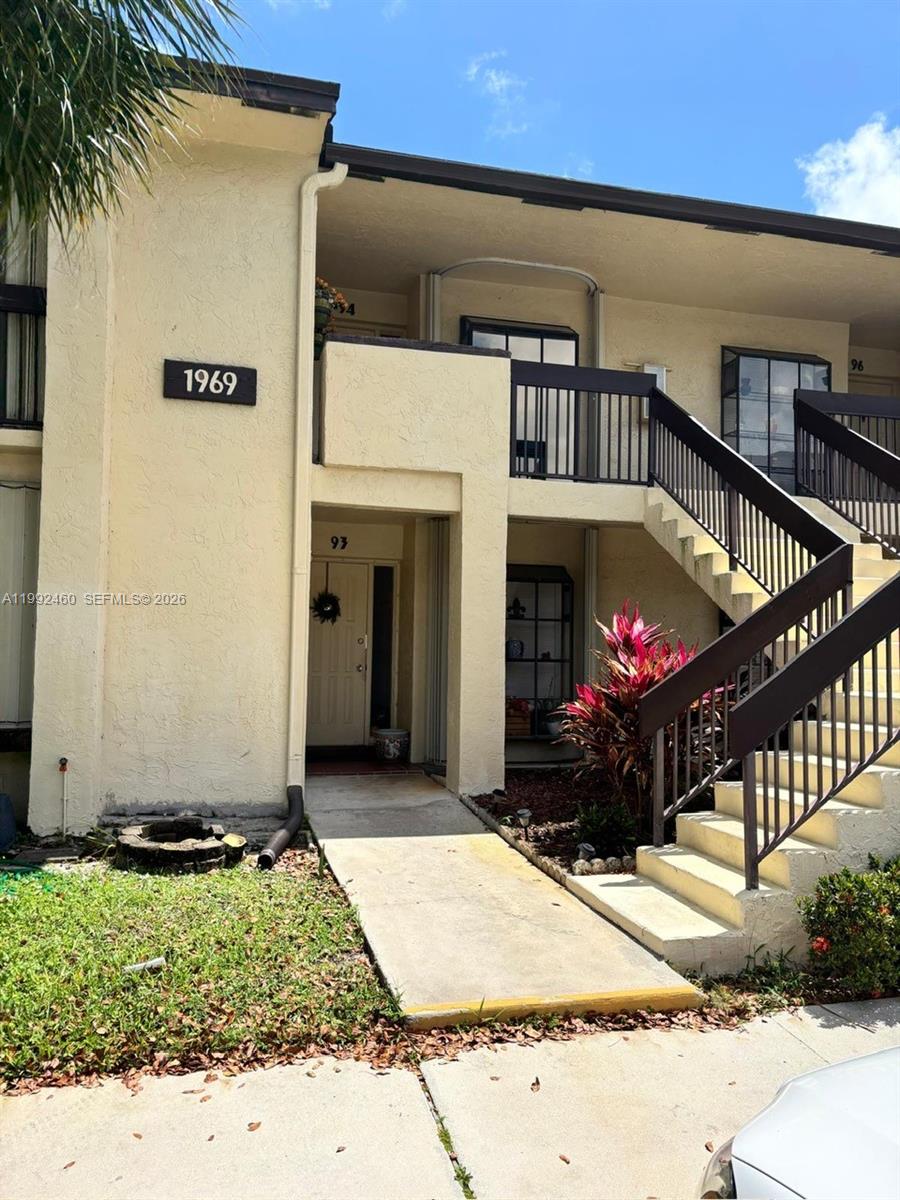 A two-story apartment building exterior features a concrete walkway, outdoor staircase, and unit numbers — 1969 SW 15th St # 93, Deerfield Beach FL 33442, DEERFIELD BEACH, FL