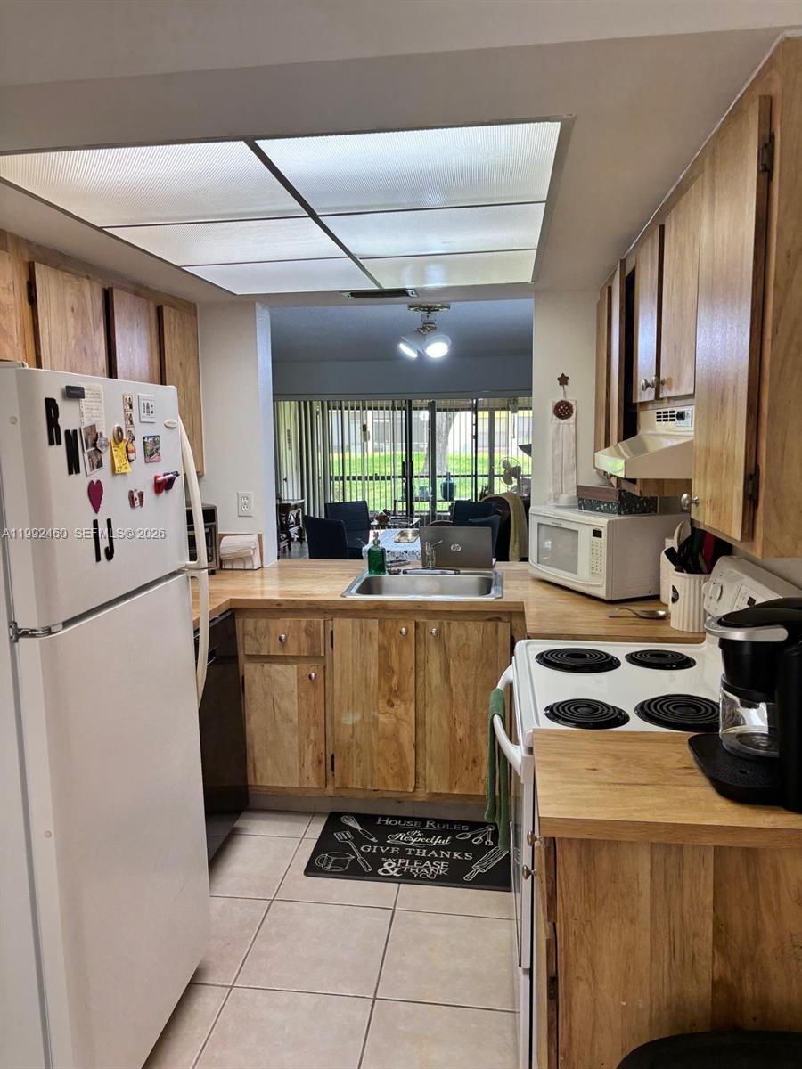 A galley kitchen features light wood cabinets, laminate countertops, and a white refrigerator — 1969 SW 15th St # 93, Deerfield Beach FL 33442, DEERFIELD BEACH, FL