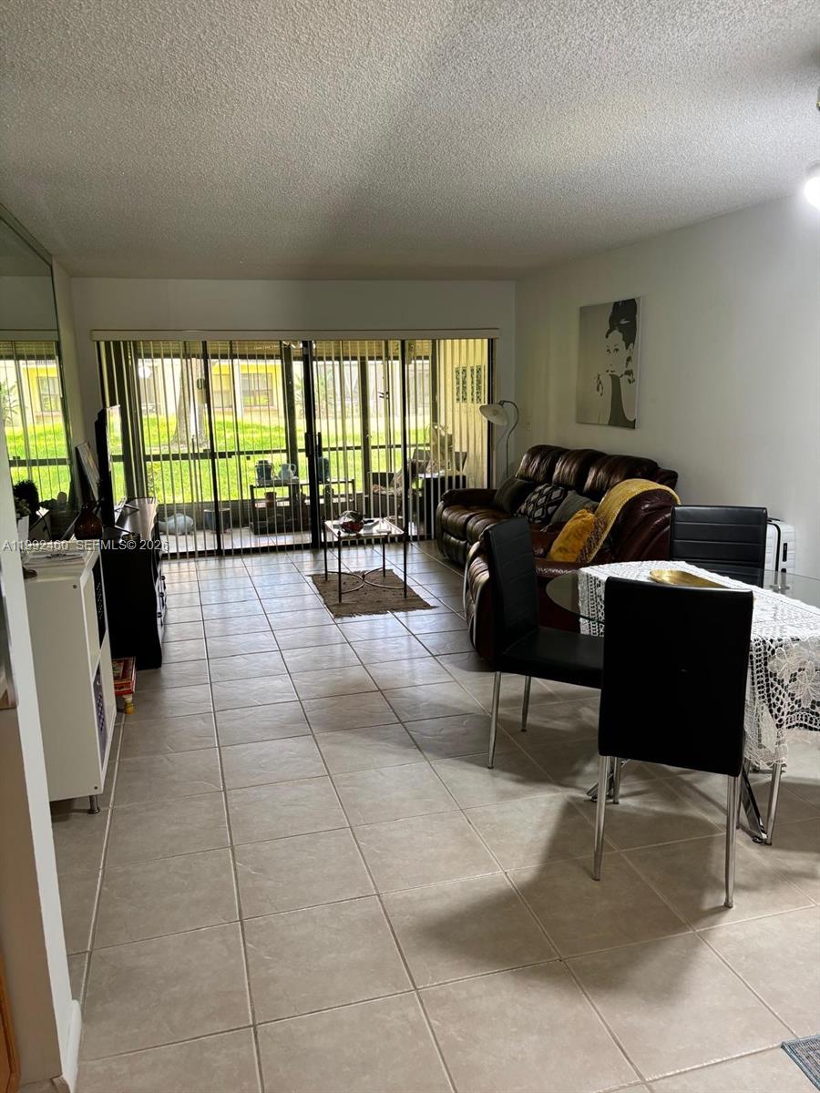 A living and dining area with tile floors, a brown leather sofa, and sliding glass doors — 1969 SW 15th St # 93, Deerfield Beach FL 33442, DEERFIELD BEACH, FL