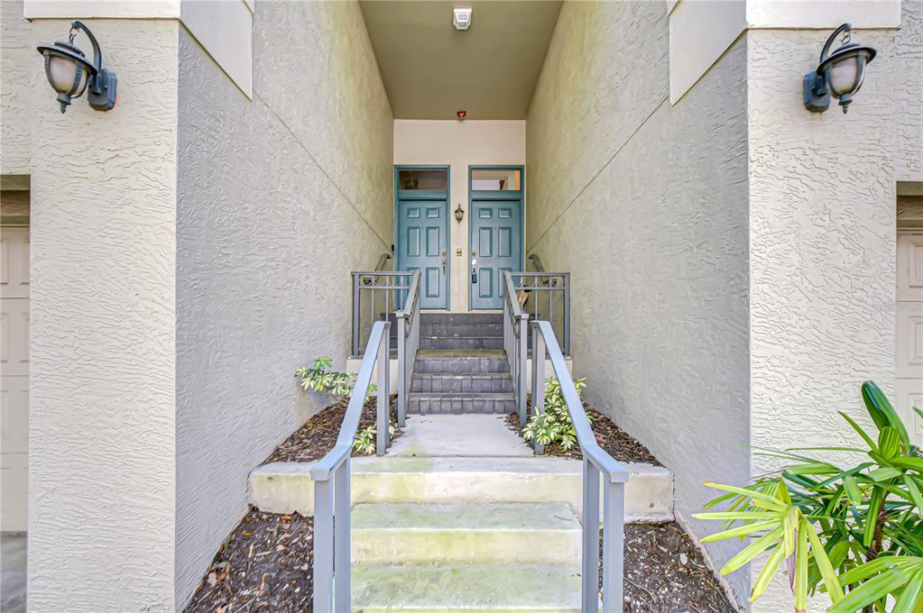 A recessed entryway features two teal front doors accessed by concrete stairs and metal railings — 609 TROPICAL BREEZE WAY UNIT 609, TAMPA, FL