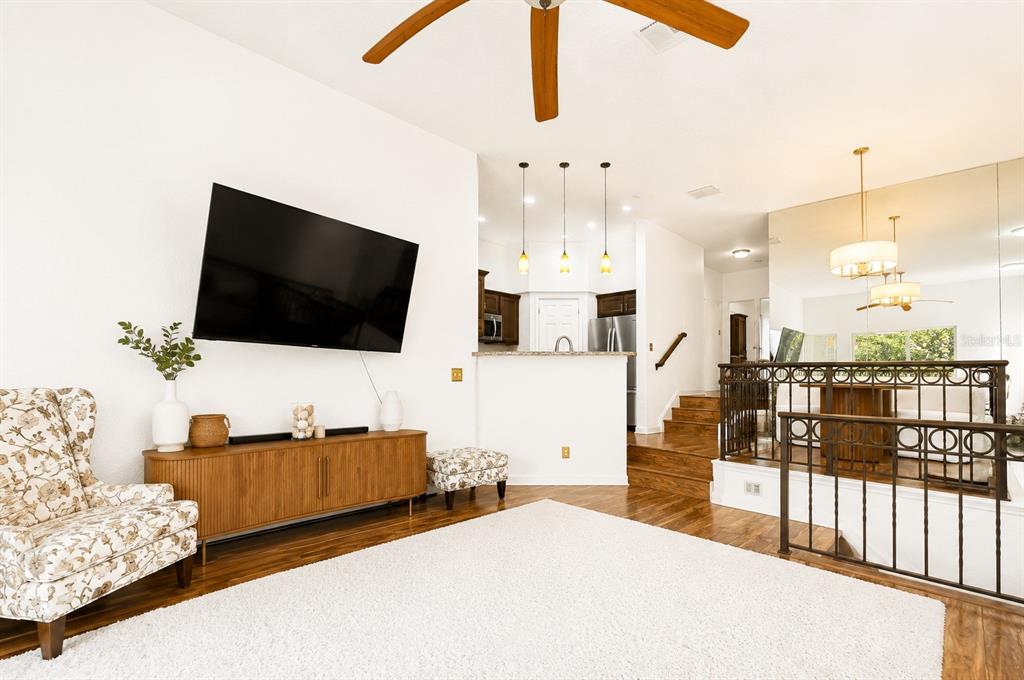 A living room with a television, wooden console, floral armchair, and stairs leading to a dining area — 609 TROPICAL BREEZE WAY UNIT 609, TAMPA, FL