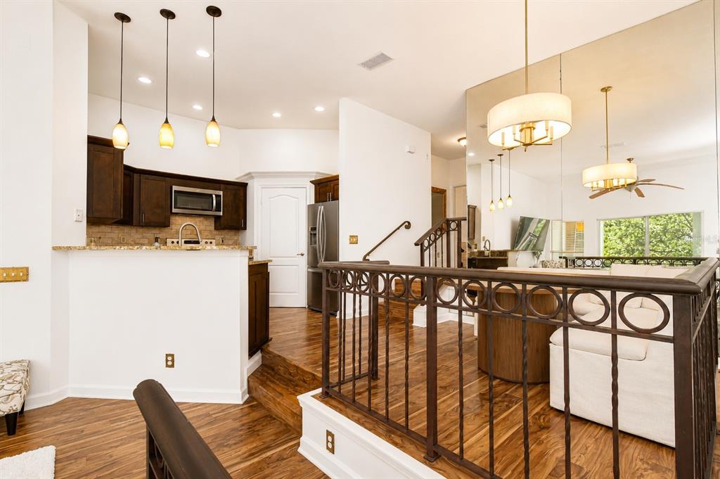A kitchen with dark cabinets and a raised living area featuring a metal railing — 609 TROPICAL BREEZE WAY UNIT 609, TAMPA, FL