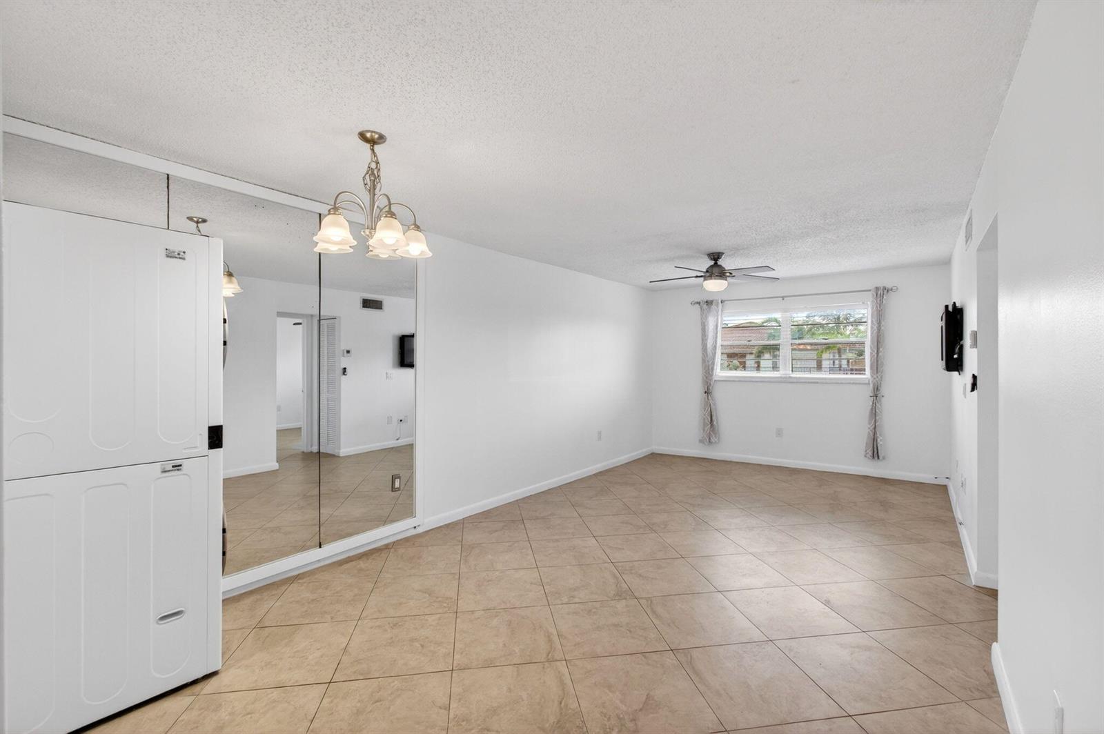 An empty room with beige tile flooring, a mirrored closet, a ceiling fan, and a window — 600 SW 2nd Avenue # 240, Boca Raton FL 33432, BOCA RATON, FL