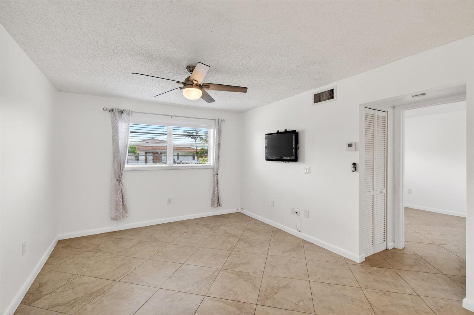 A room with white walls, tile flooring, a ceiling fan, and a wall-mounted television — 600 SW 2nd Avenue # 240, Boca Raton FL 33432, BOCA RATON, FL