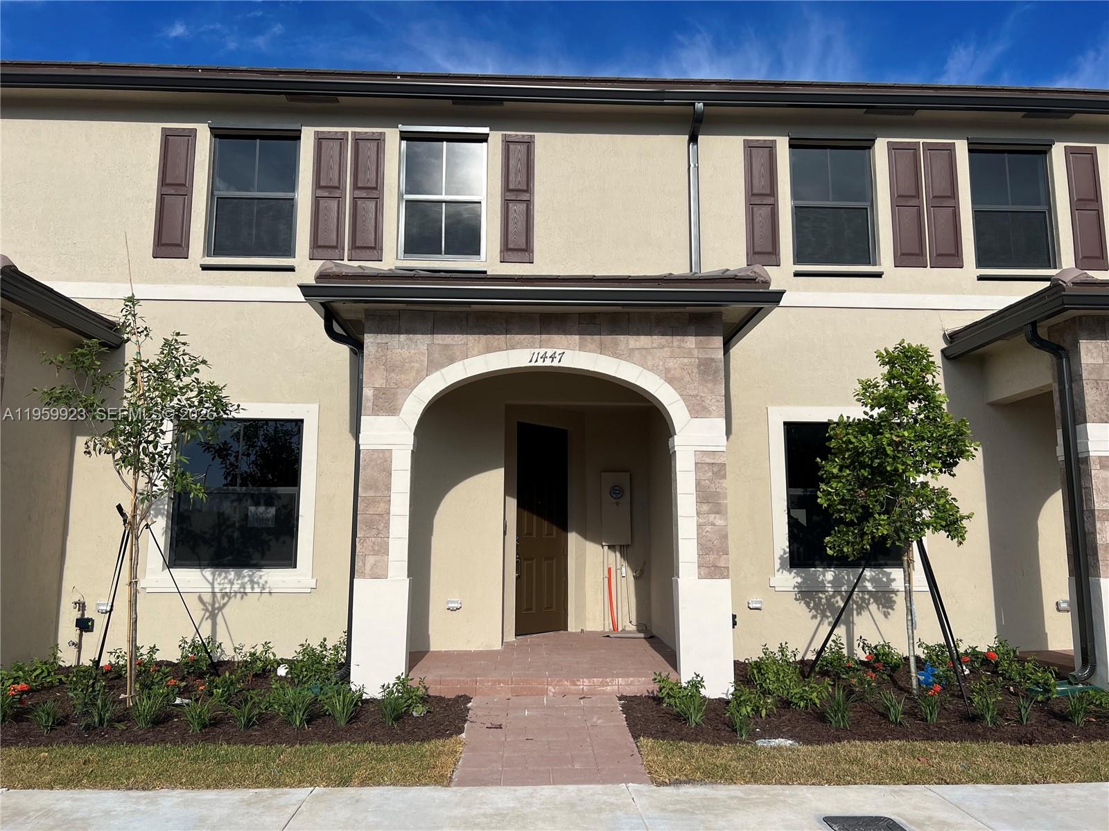 A two-story townhouse exterior features a stone-accented arched entryway and brown shutters — 11447 W 34th Ct, Hialeah FL 33018, HIALEAH, FL