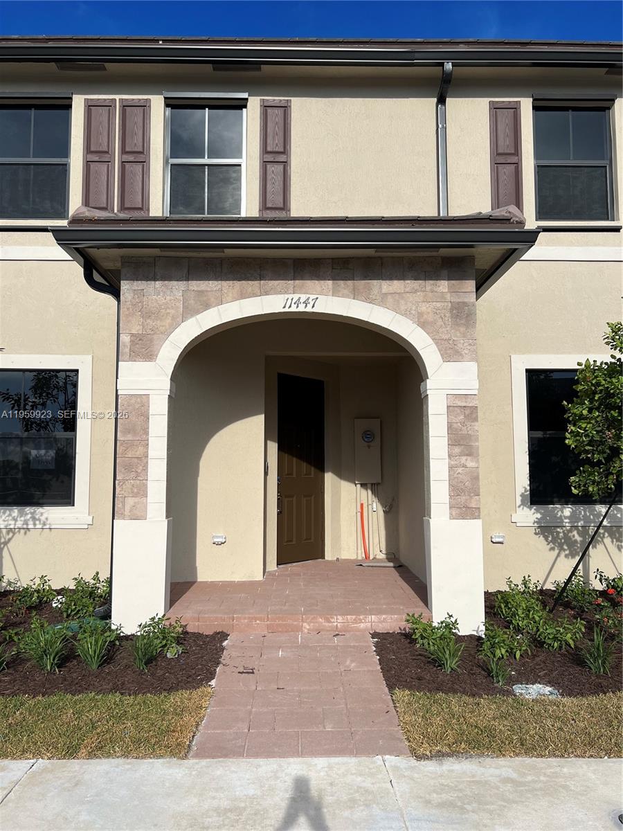 The exterior of a two-story townhouse features a stone-accented arched entryway and a brown door — 11447 W 34th Ct, Hialeah FL 33018, HIALEAH, FL