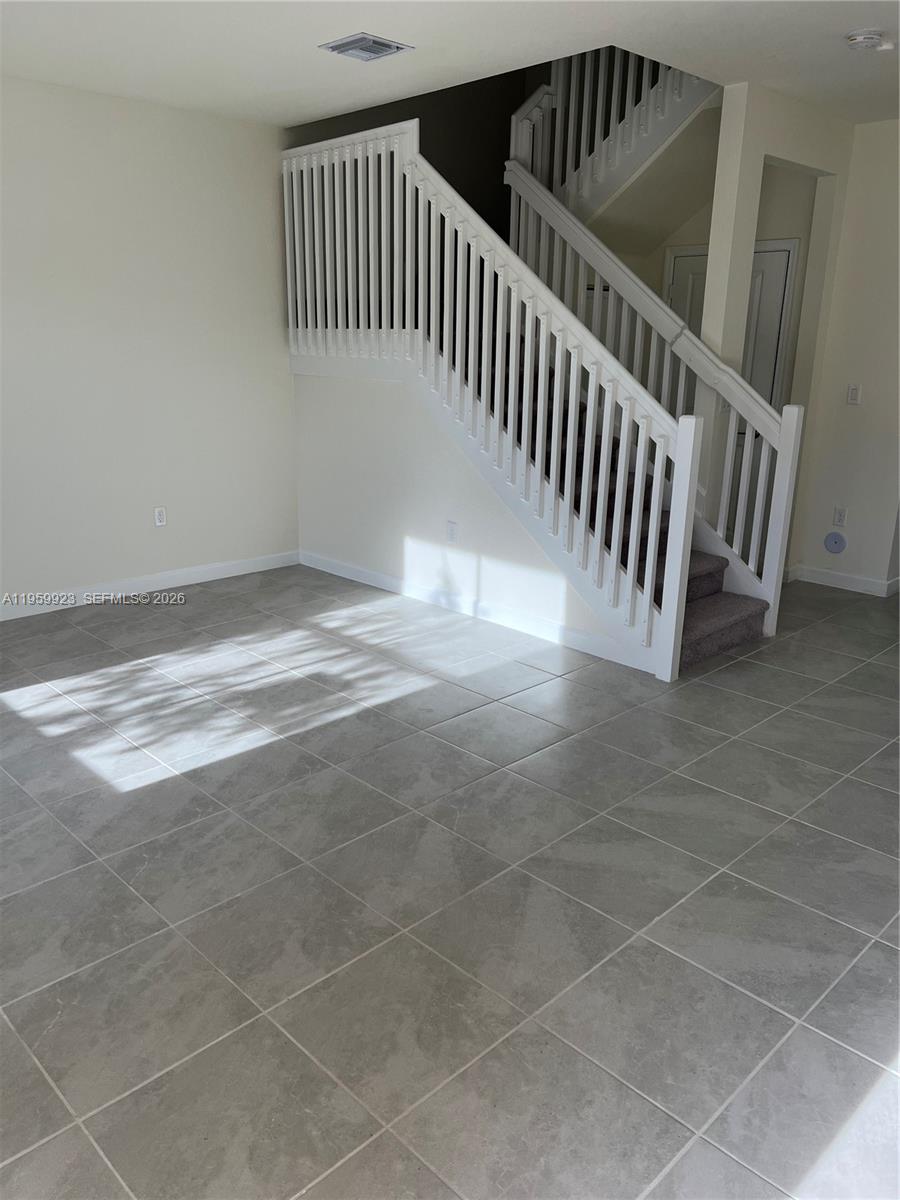 A room with light-colored tile flooring features a white wooden staircase leading upstairs — 11447 W 34th Ct, Hialeah FL 33018, HIALEAH, FL