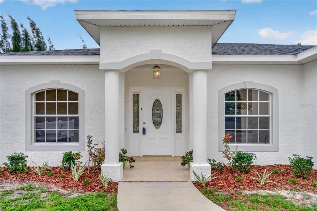 The exterior of a white house features a covered entryway with two columns and windows — 6026 113TH AVENUE N, PINELLAS PARK, FL