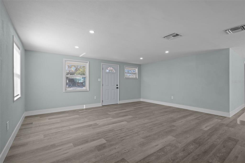 An empty room with light blue walls, gray wood-look flooring, and a white front door — 1682 WILMAR AVENUE, TARPON SPRINGS, FL