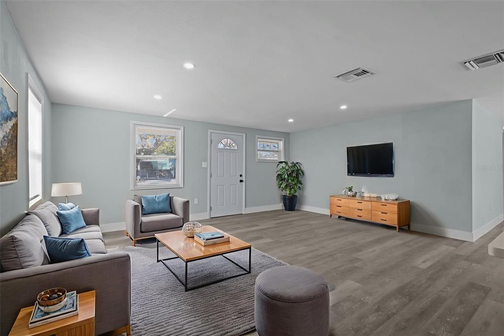 A living room features light gray walls, wood-look flooring, a gray sofa, and a television — 1682 WILMAR AVENUE, TARPON SPRINGS, FL