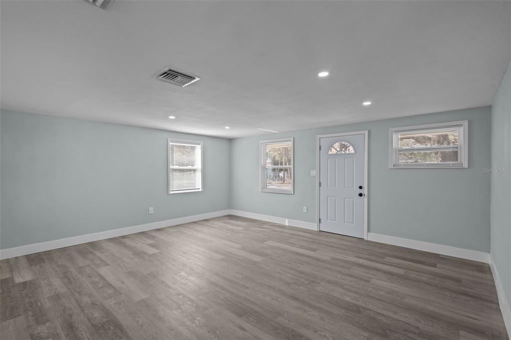 An empty room with light blue walls, gray wood-look flooring, recessed lighting, and a white door — 1682 WILMAR AVENUE, TARPON SPRINGS, FL