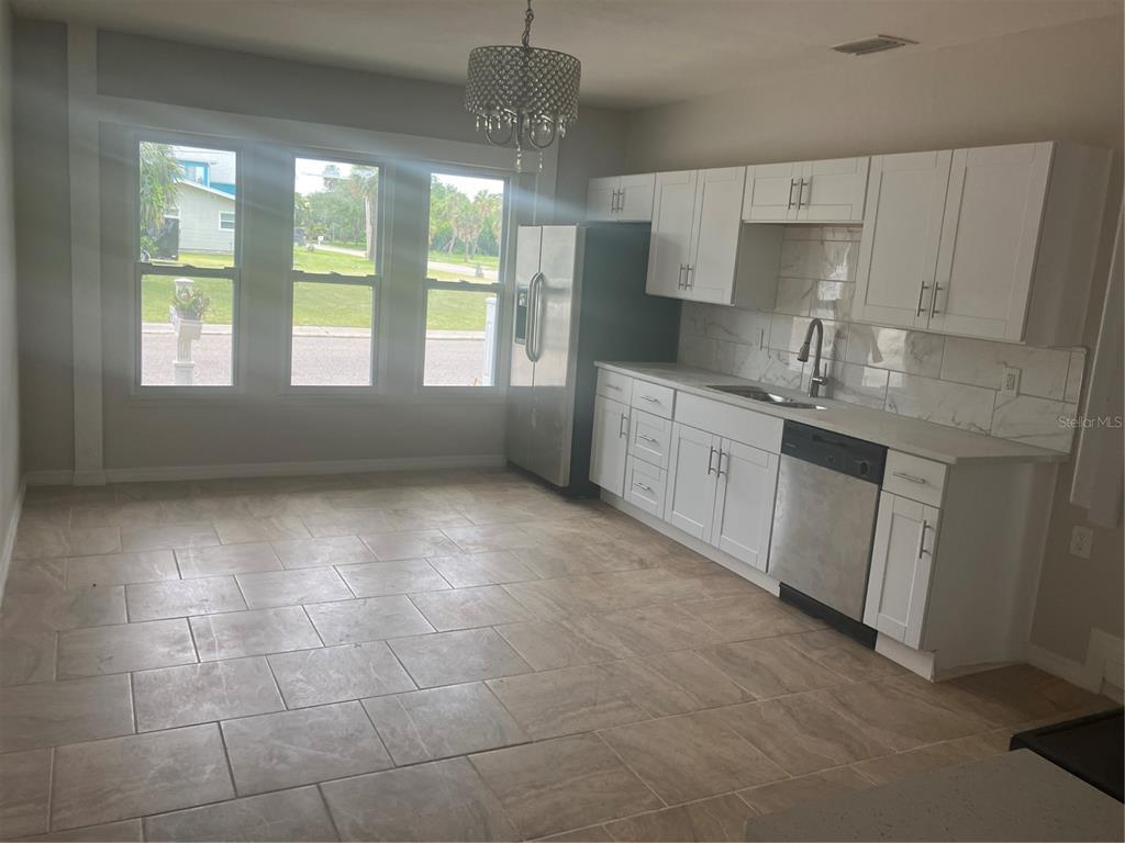 A kitchen features white cabinets, stainless steel appliances, tile flooring, and three large windows — 601 BANANA STREET, TARPON SPRINGS, FL