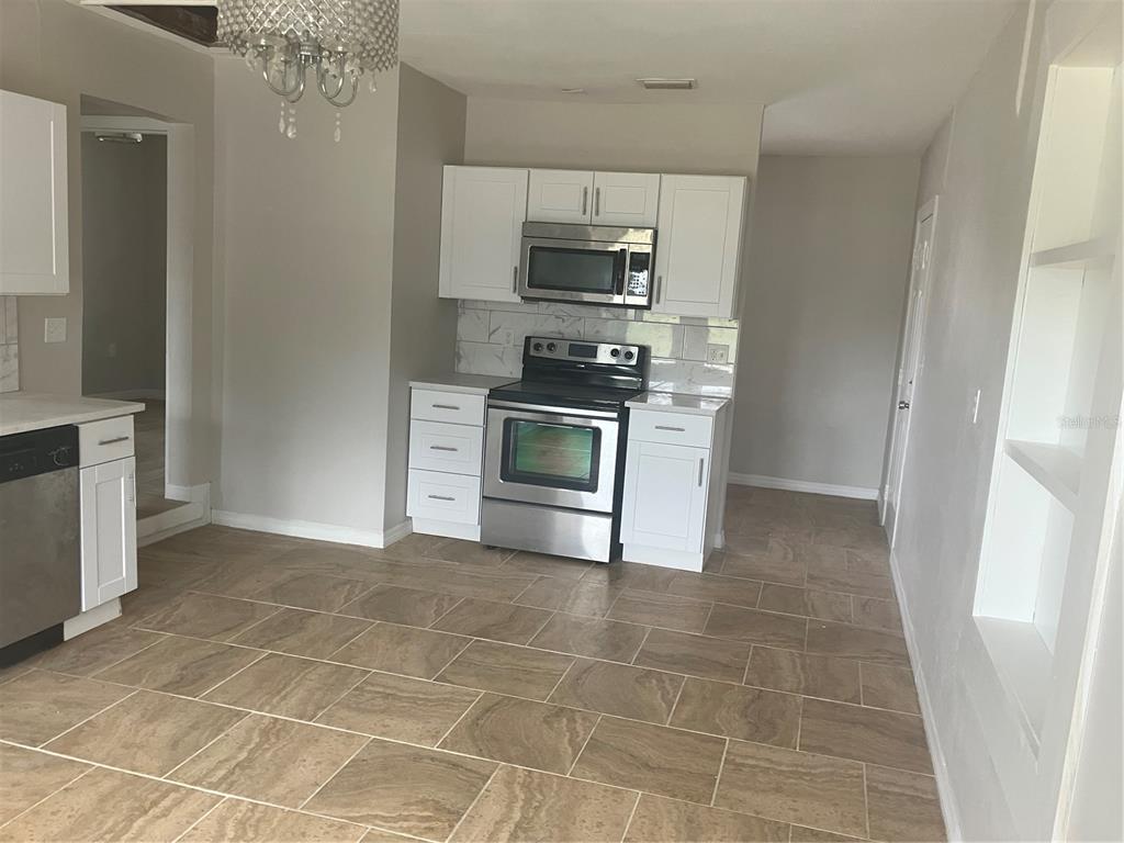 A kitchen features white cabinets, stainless steel appliances, a marble-style backsplash, and tan tile flooring — 601 BANANA STREET, TARPON SPRINGS, FL