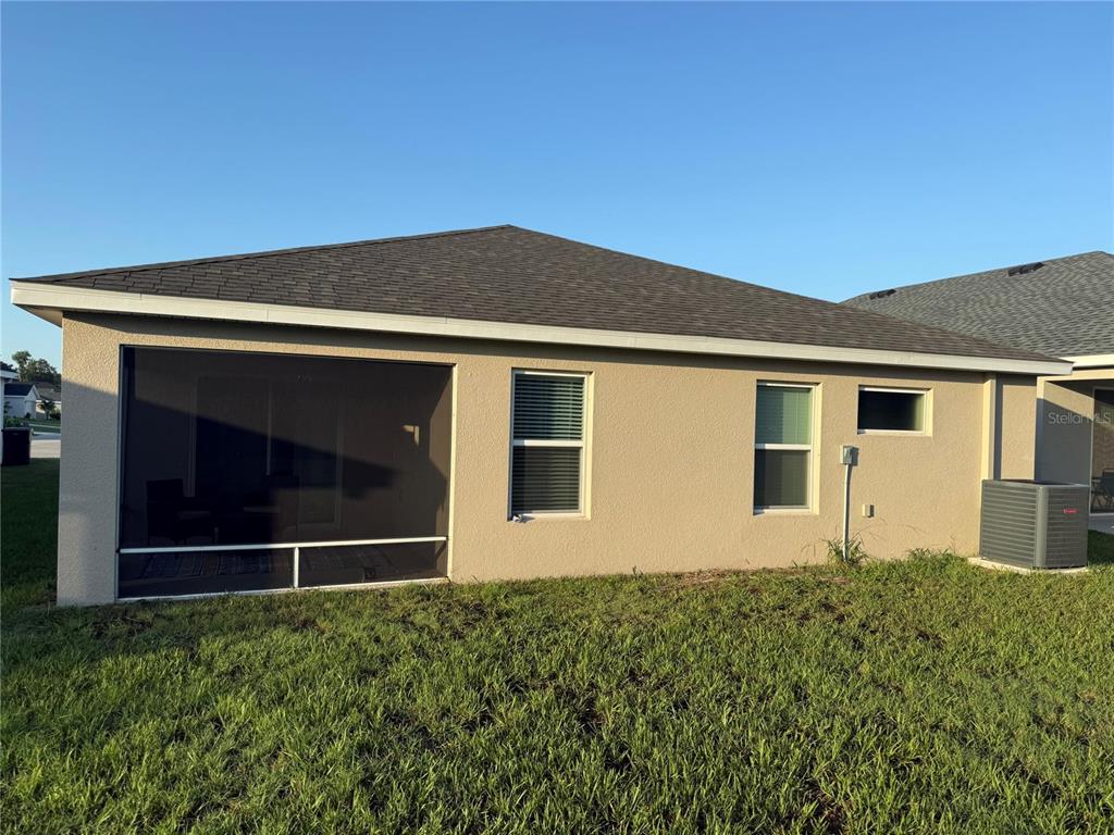 The exterior rear view of a tan stucco house features a screened-in porch and windows — 615 BENTLEY NORTH DRIVE, AUBURNDALE, FL