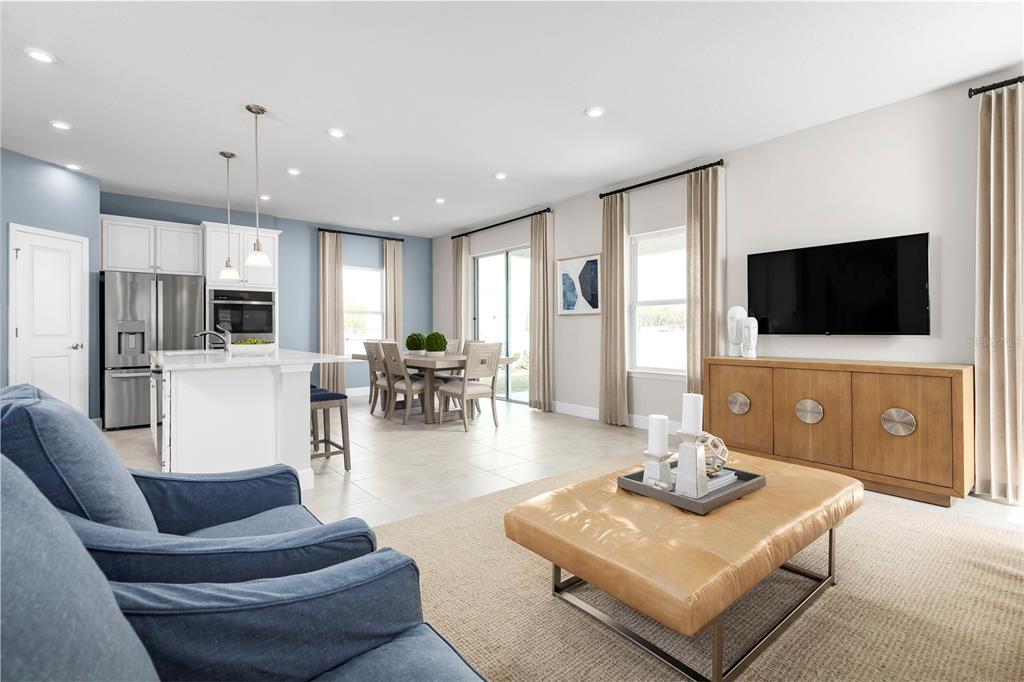 An open-concept living room and kitchen featuring a blue sofa, dining area, and television console — 2437 WHITE LADYFISH ROAD, WIMAUMA, FL