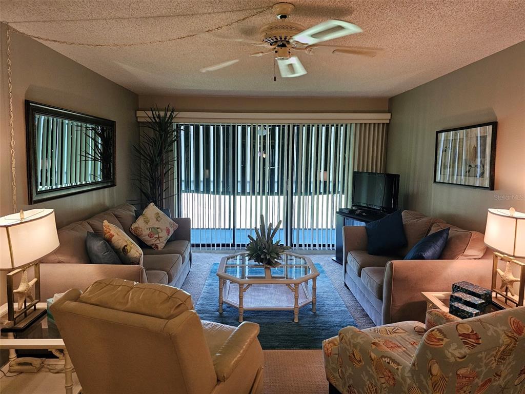 A living room features two sofas, a patterned armchair, a coffee table, and vertical blinds — 4119 61ST AVENUE TERRACE W UNIT 303, BRADENTON, FL