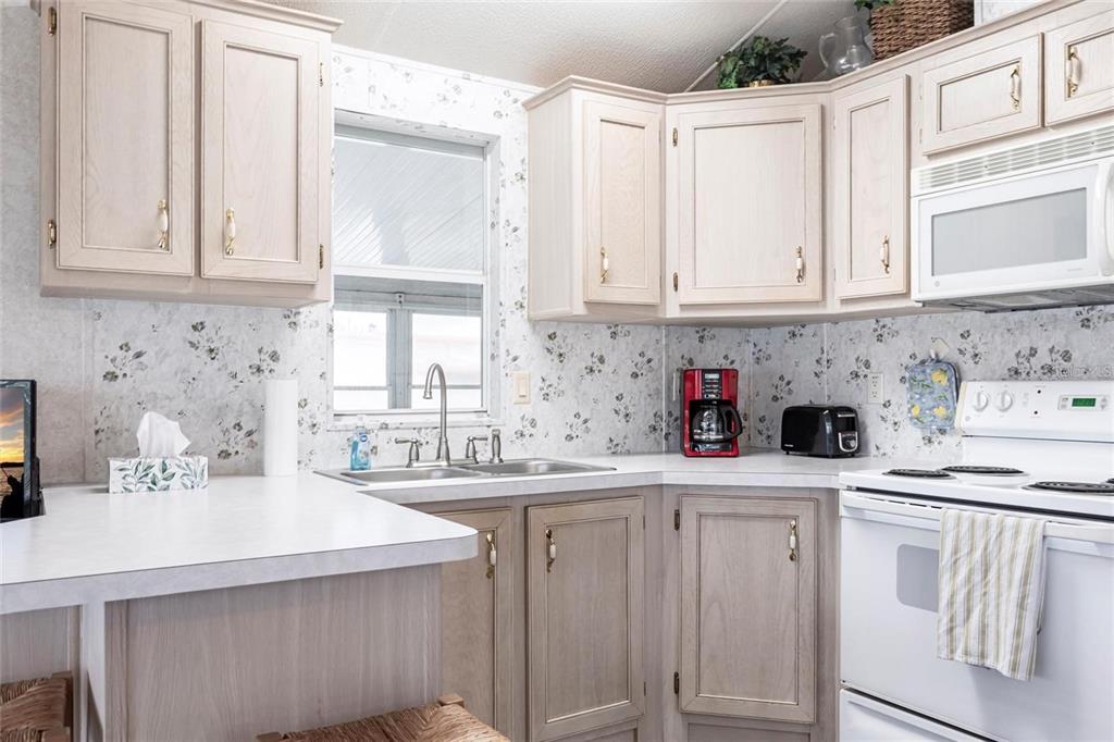 A kitchen features light wood cabinets, white countertops, floral wallpaper, and white appliances — 1604 N MANATEE LOOP, PUNTA GORDA, FL
