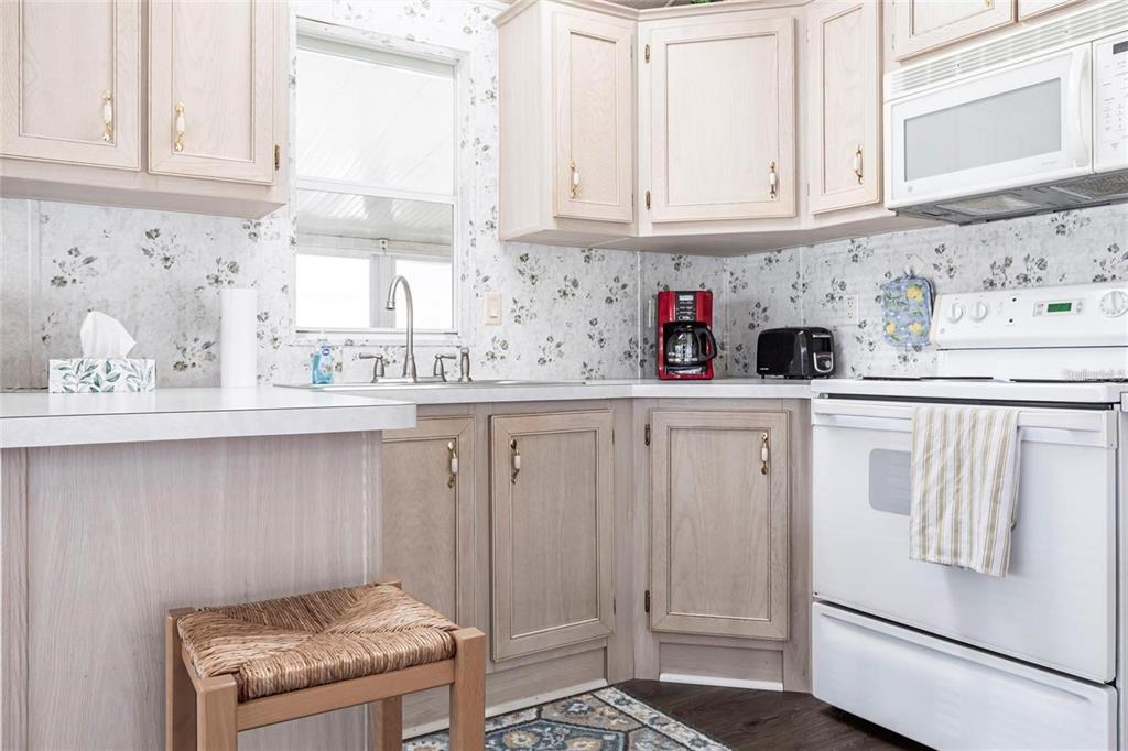 A kitchen features light wood cabinets, floral wallpaper, white appliances, and a small wooden stool — 1604 N MANATEE LOOP, PUNTA GORDA, FL
