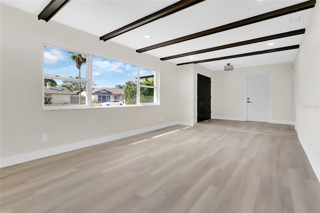 A bright living room features light wood-look flooring, dark ceiling beams, and a large window — 330 ELKHORN COURT, WINTER PARK, FL