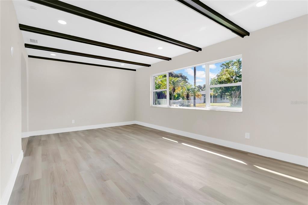 A bright room features light wood-look flooring, white walls, and dark exposed ceiling beams — 330 ELKHORN COURT, WINTER PARK, FL