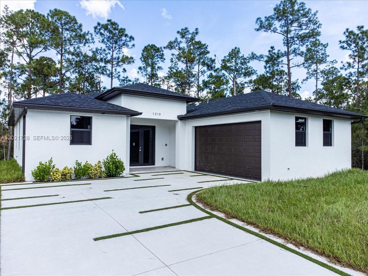 A modern white single-story house features a dark garage door and a concrete driveway — 1310 Jefferson Ave, Lehigh Acres FL 33972, LEHIGH ACRES, FL