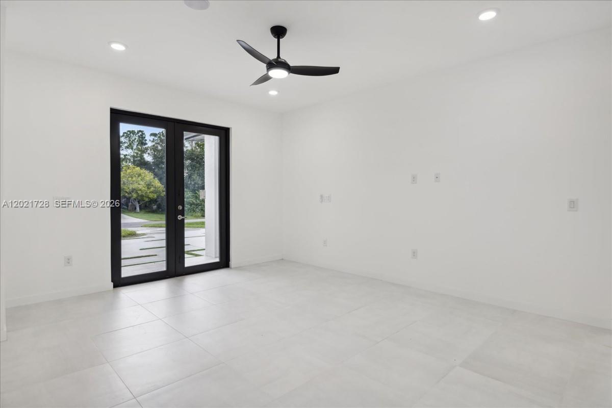 A minimalist room features white walls, large light-colored floor tiles, and black French doors — 1310 Jefferson Ave, Lehigh Acres FL 33972, LEHIGH ACRES, FL