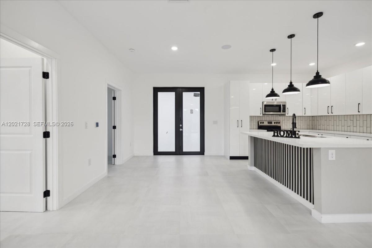 A modern kitchen features white cabinetry, a slatted island, and black pendant lighting — 1310 Jefferson Ave, Lehigh Acres FL 33972, LEHIGH ACRES, FL