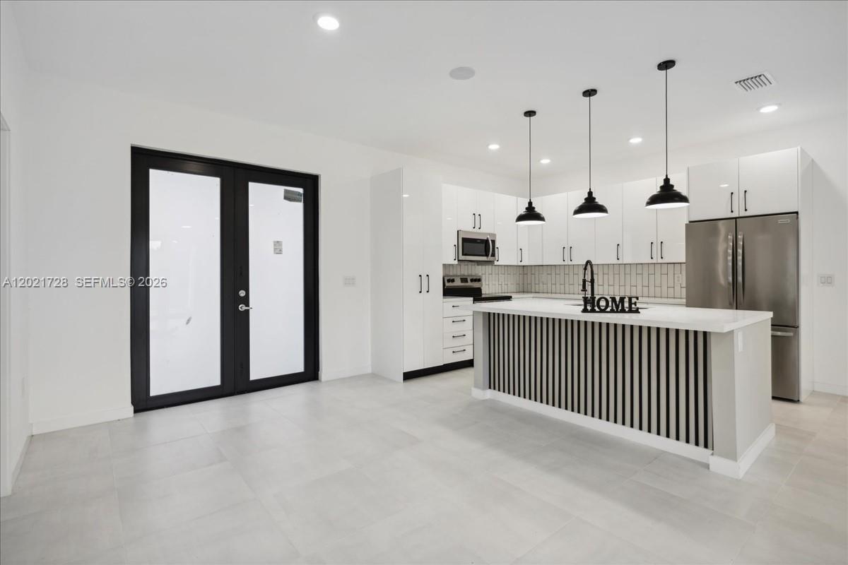 A modern kitchen features white cabinetry, a slatted island, stainless steel appliances, and tile flooring — 1310 Jefferson Ave, Lehigh Acres FL 33972, LEHIGH ACRES, FL
