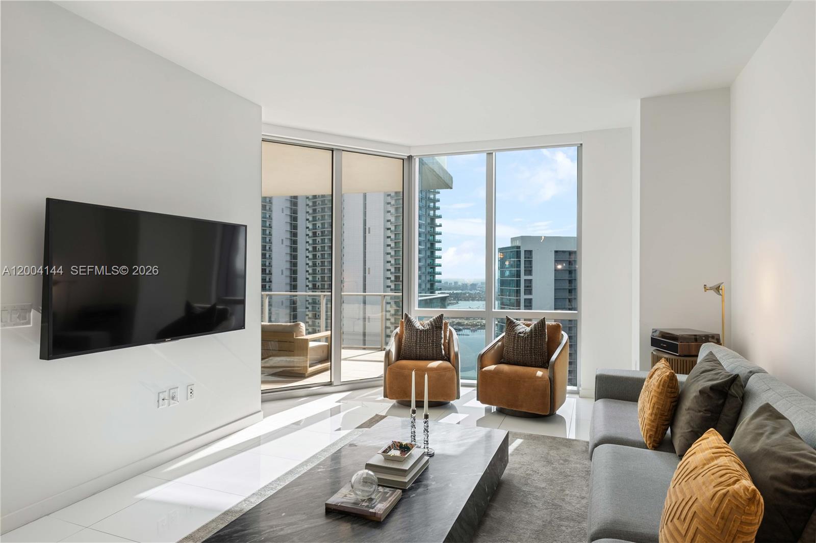 A modern living room features a wall-mounted television, gray sofa, and floor-to-ceiling windows — 851 NE 1st Ave # 4405, Miami FL 33132, MIAMI, FL