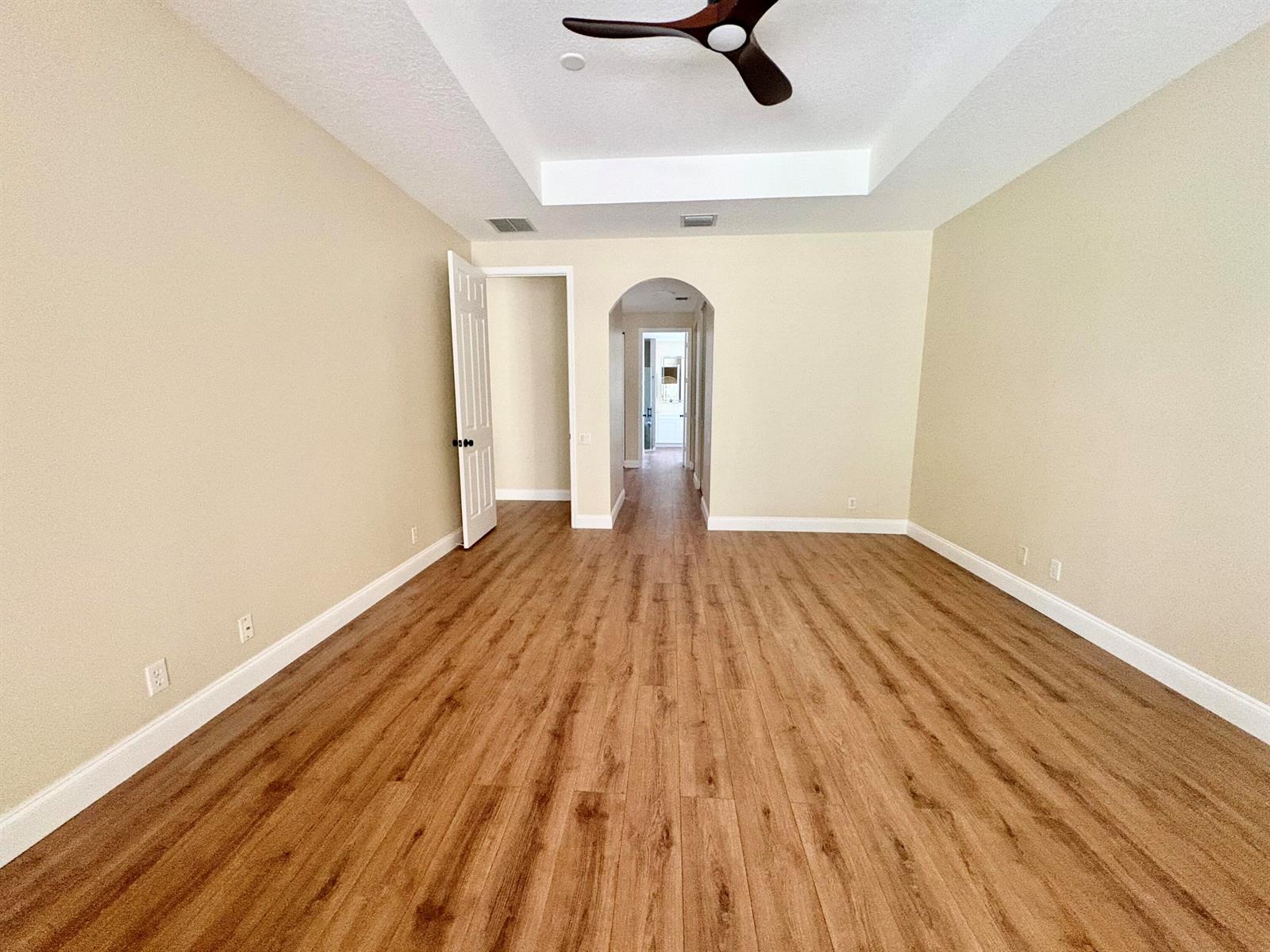 An empty room with wood-look flooring, a tray ceiling with a fan, and arched doorways — 8958 Terni Lane, Boynton Beach FL 33472, BOYNTON BEACH, FL