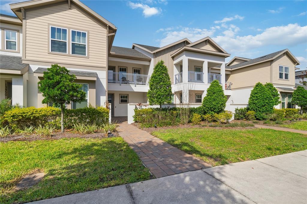 A two-story townhouse exterior features tan siding, a brick walkway, and second-floor balconies — 13444 STODDART AVENUE, ORLANDO, FL