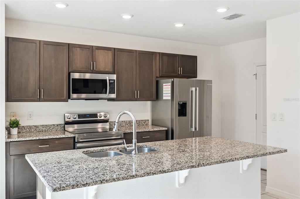 A kitchen features dark wood cabinets, granite countertops, stainless steel appliances, and a central island — 1995 5TH AVENUE, DELAND, FL