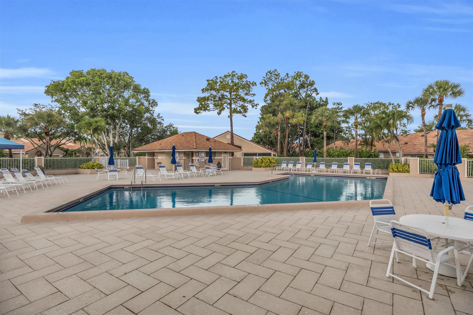 A swimming pool with lounge chairs and umbrellas on a paved deck at a complex — 1105 Duncan Circle # 104, Palm Beach Gardens FL 33418, PALM BEACH GARDENS, FL