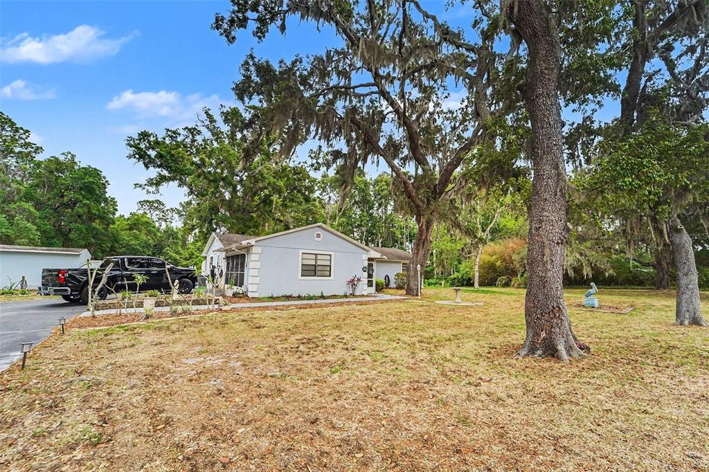 A light-colored house with a black pickup truck parked in the driveway under large trees — 13020 SUGAR CREEK BOULEVARD, HUDSON, FL